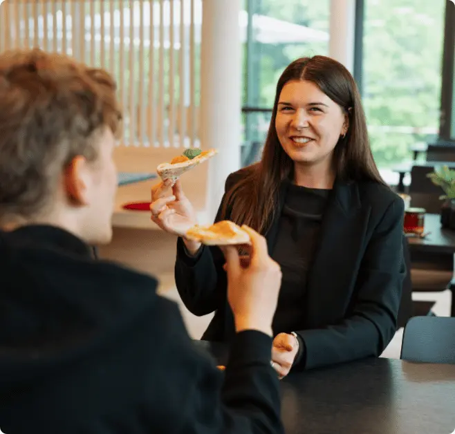 Zwei lächelnde Menschen die zusammen Pizza essen.