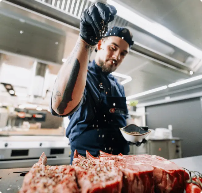 Koch der Gewürze auf ein frisches Stück Steak rieseln lässt.