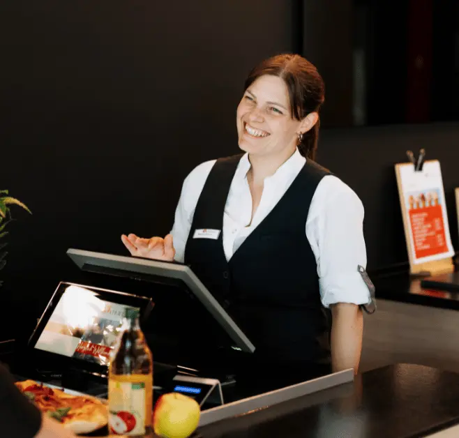 Lächelnde Frau, die an der Kasse steht und einen Kunden bedient.